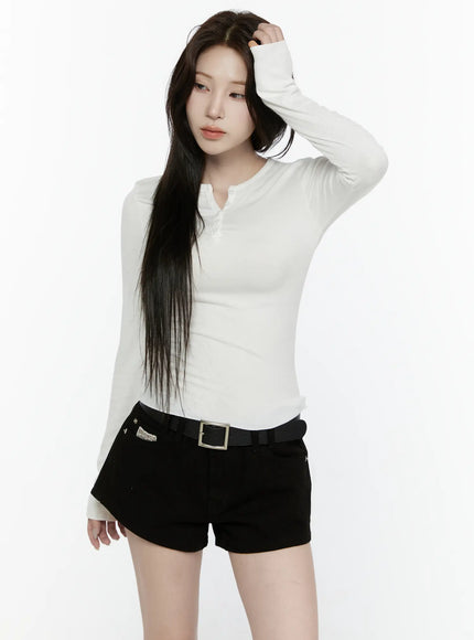Button-Up Long Sleeve Top IL521 White front shot on model with one hand raised to hair, slim ribbed henley long sleeve top with button placket, styled with black belted shorts