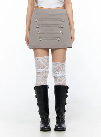 Buttoned Mini Skirt CL517 Beige front mid-body shot on model showing full button panel and waistband with lace socks and black buckle boots