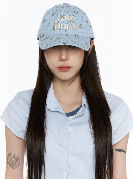 LEWKIN Camden Flower Ball Cap IL503 light blue front view on model wearing brim low over eyes with blue striped shirt, denim floral pattern with cream Love Dune embroidery