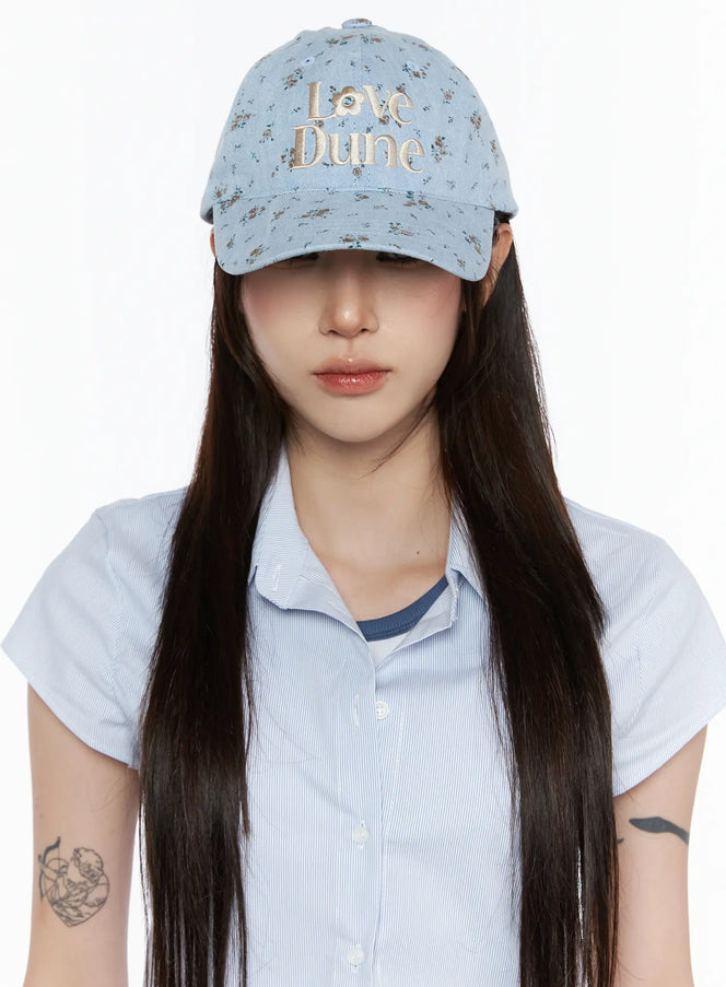LEWKIN Camden Flower Ball Cap IL503 light blue front view on model wearing brim low over eyes with blue striped shirt, denim floral pattern with cream Love Dune embroidery