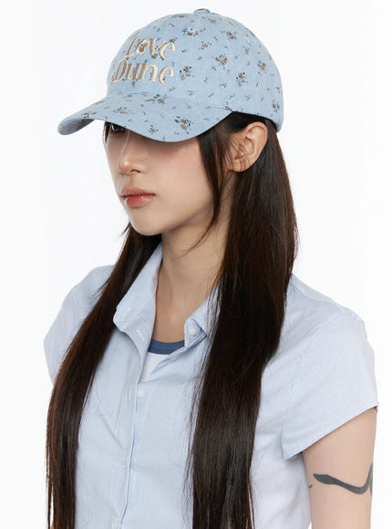Camden Flower Ball Cap IL503 light blue three-quarter front view on model with long dark hair, floral denim fabric and cream Love Dune embroidery detail visible