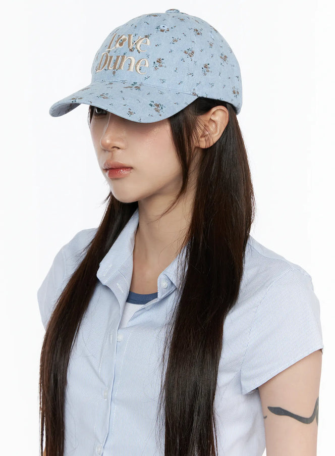 Camden Flower Ball Cap IL503 light blue three-quarter front view on model with long dark hair, floral denim fabric and cream Love Dune embroidery detail visible