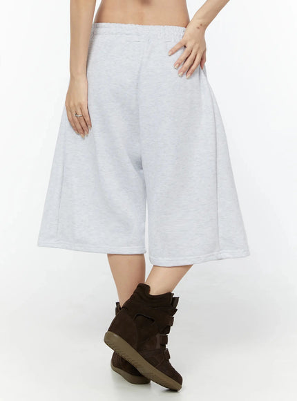 Camo Cross Patch Bermuda Shorts IU524 Light gray full-body front shot on model styled with black crop tee, tan cap and black handbag, walking pose with brown wedge sneakers