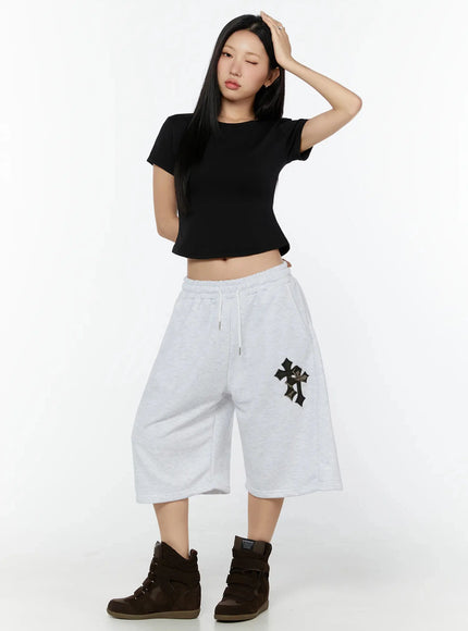 Camo Cross Patch Bermuda Shorts IU524 Light gray full-body front shot on model with hand raised to head, paired with black crop tee and brown wedge sneakers