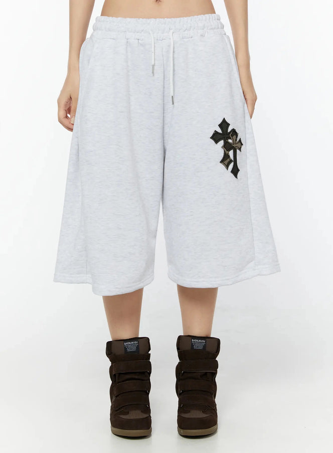 LEWKIN Camo Cross Patch Bermuda Shorts IU524 Light gray front view on model, cropped waist shot, wide-leg fleece shorts with black camo cross appliqué patch and white drawstring