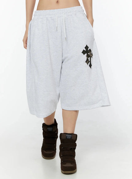 Camo Cross Patch Bermuda Shorts IU524 Light gray front cropped view on model walking forward, wide-leg fleece shorts with camo cross patch and white drawstring waist