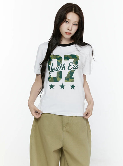 Camo Graphic T-Shirt IL522 White upper-body front close-up on model without cap showing black ringer crewneck and green camouflage 07 Youth Era graphic print