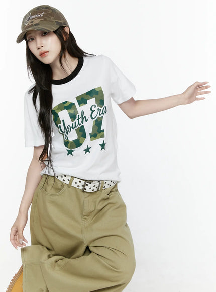 LEWKIN Camo Graphic T-Shirt IL522 White S/M front angled shot on model seated pose wearing camo cap black ringer neckline camouflage 07 Youth Era print