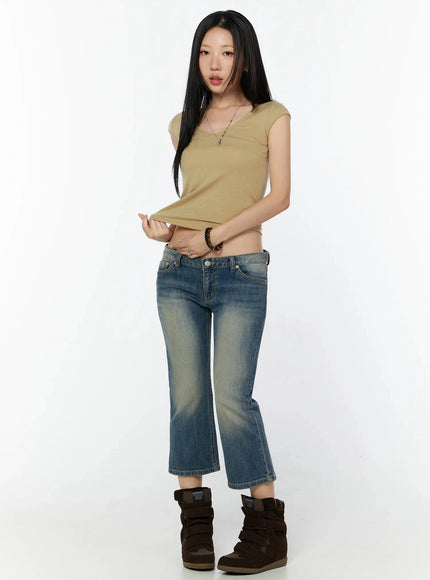 Cap Sleeve V-Neck Top IL516 Beige three-quarter front shot model standing lifting hem of cropped top styled with low-rise flare jeans