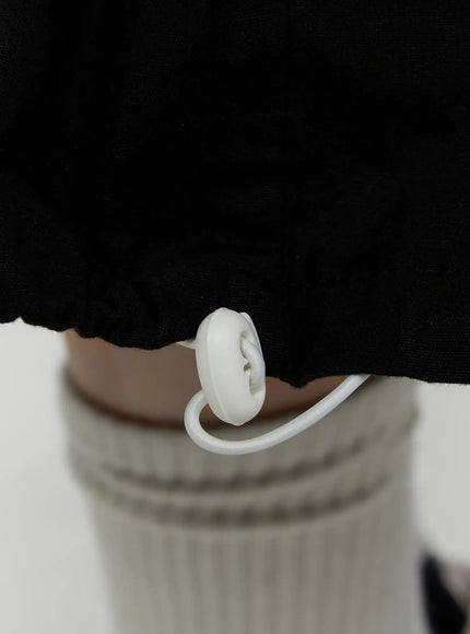 Cargo Pocket Shorts IL521 Black close-up detail of white plastic drawstring toggle stopper at hem with raw-edge finish