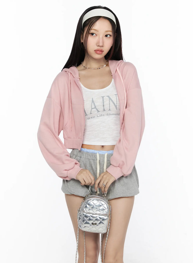 LEWKIN Casual Cropped Hoodie CL527 Light pink front shot on model size S/M open zip hoodie styled with graphic crop top and gray shorts holding silver quilted mini bag