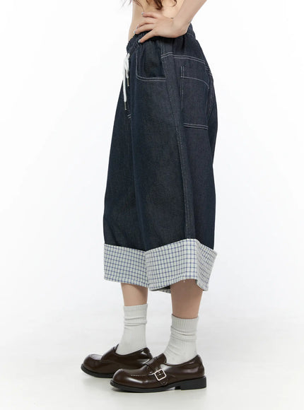 Check Back Pocket Jorts CL522 Dark blue side view on model showing drawstring elastic waist, wide-leg denim body, contrast topstitching, and rolled plaid check cuff hem detail