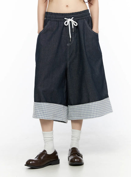 Check Back Pocket Jorts CL522 Dark blue front view on model showing wide-leg dark indigo denim, white drawstring elastic waist, contrast stitching, and wide plaid check turn-up cuff hem