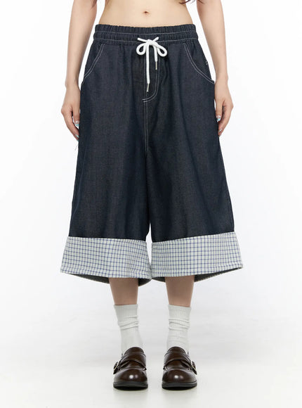 Check Back Pocket Jorts CL522 Dark blue front view on model wearing yellow graphic tee showing white drawstring waist, wide-leg dark denim with plaid check turn-up cuff hem