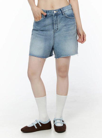 Classic Washed Jorts IU525 Blue front 3/4 view on model with hand in pocket, showing faded wash, five-pocket design, and frayed hem denim shorts