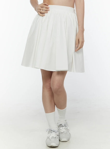 Colette A-Line Midi Skirt IL506 White three-quarter front view on model showing pleated high-waist A-line skirt with hand on hip white socks and sneakers