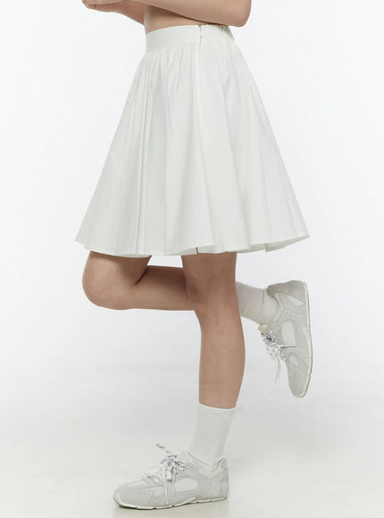 Colette A-Line Midi Skirt IL506 White side view on model with one leg raised showing voluminous pleated A-line skirt flare and zipper detail at waistband