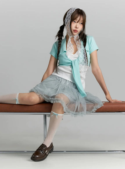 Collared Tie Short Sleeve Crop Bolero CL514 Mint seated lifestyle shot model on bench wearing mint bolero with lace headscarf white eyelet inner top gray tulle skirt and loafers