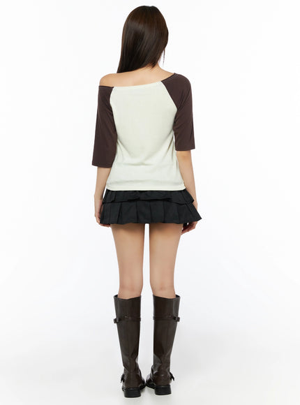 Color Block Off-Shoulder Tee IL523 Yellow full-length back shot on model, cream body with dark brown raglan sleeves, contrast topstitching at shoulder seam, styled with black tiered mini skirt and boots
