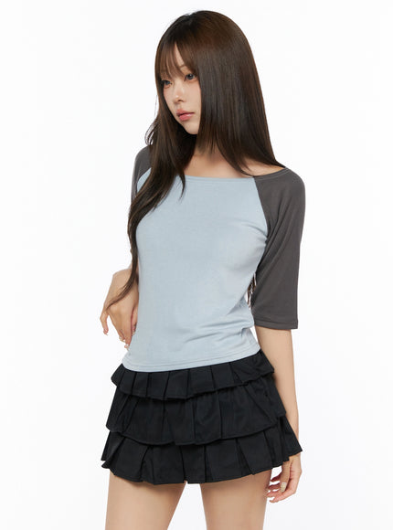 Color Block Off-Shoulder Tee IL523 Blue three-quarter front shot on model, light blue body with charcoal gray raglan sleeves, fitted knit texture, paired with black tiered mini skirt