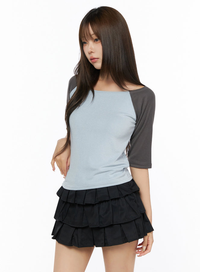 Color Block Off-Shoulder Tee IL523 Blue three-quarter front shot on model, light blue body with charcoal gray raglan sleeves, fitted knit texture, paired with black tiered mini skirt