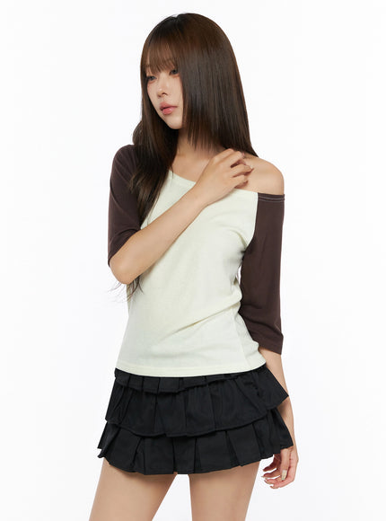 Color Block Off-Shoulder Tee IL523 Yellow angled front shot on model touching shoulder, cream body with dark brown raglan half sleeves, off-shoulder style, paired with black tiered mini skirt