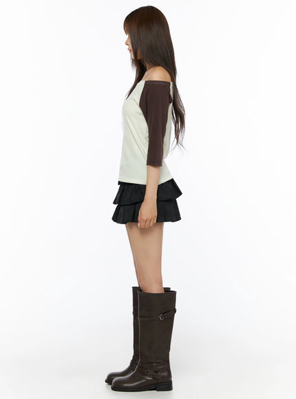 Color Block Off-Shoulder Tee IL523 Yellow full-length side shot on model, cream body with dark brown raglan sleeve profile, off-shoulder silhouette, paired with black tiered skirt and brown boots