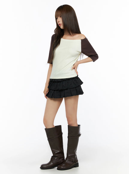 Color Block Off-Shoulder Tee IL523 Yellow full-length angled shot on model, cream body with dark brown raglan sleeves, hand on hip, paired with black tiered mini skirt and brown knee-high boots