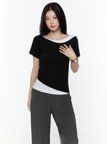 Color Contrast Asymmetric Short Sleeve Top IL506 Black front shot on model with hand on chest showing white contrast neckline and asymmetric diagonal hem detail