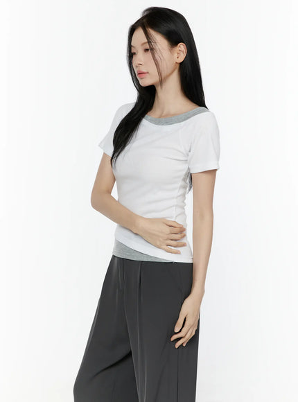 Color Contrast Asymmetric Short Sleeve Top IL506 White three-quarter side shot on model looking down, hand on waist, showing ribbed body and gray contrast hem
