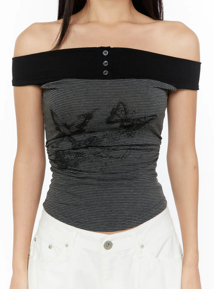 Color Contrast Off-Shoulder Graphic Top CU529 Dark gray close-up front model shot detailing black off-shoulder band with snap buttons butterfly graphic print on ruched gray striped knit