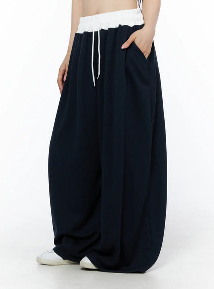 Color Contrast Wide-Leg Sweatpants IU525 Dark blue side view on model with hand in pocket, voluminous wide-leg drape and white contrast waistband visible