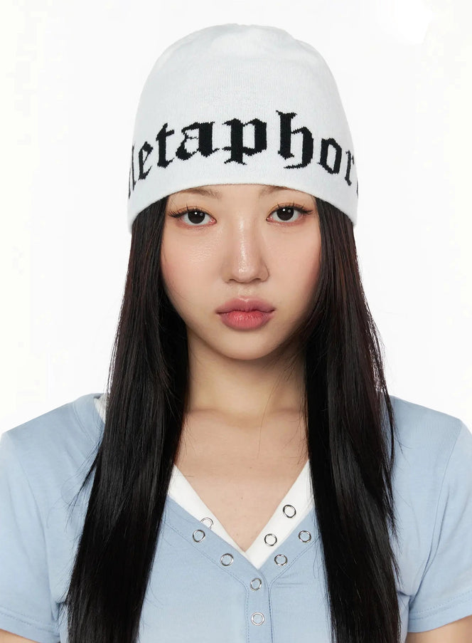 LEWKIN Contrast Graphic Text Reversible Beanie IL516 White front model shot, female wearing knit beanie with gothic black Metaphor's lettering, styled with blue v-neck top