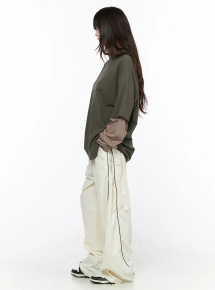 Contrast Piping Nylon Wide Pants CL523 Light beige full-length side styling shot model in olive tee hands in pockets profile pose
