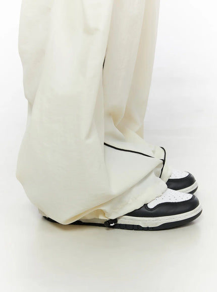 Contrast Piping Nylon Wide Pants CL523 Light beige close-up detail of hem pooling over sneakers with black piping drawstring at ankle