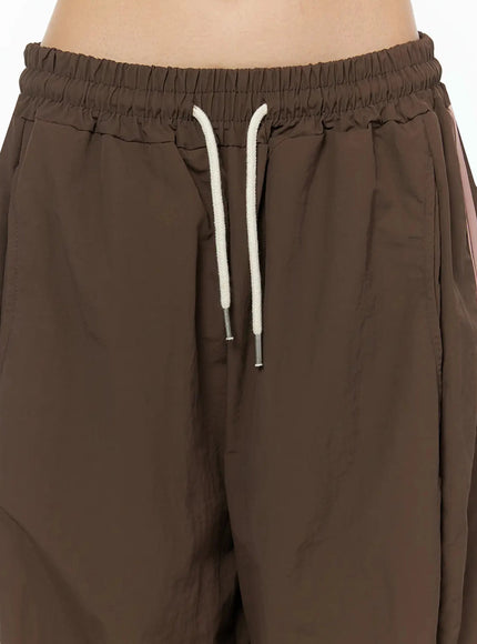 Contrast Stripe Track Pants IL509 Brown close-up detail of elastic waistband and cream rope drawstring with silver aglets on model, nylon texture visible
