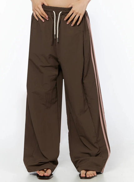 LEWKIN Contrast Stripe Track Pants IL509 Brown S/M front close-up on model showing cream drawstring elastic waistband and pink side stripes, nylon fabric