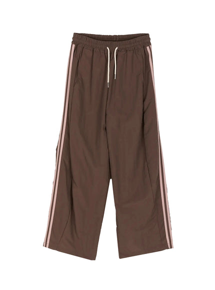 Contrast Stripe Track Pants IL509 Brown flat-lay front view showing full wide-leg shape, cream drawstring waistband and dual pink side stripes on nylon fabric