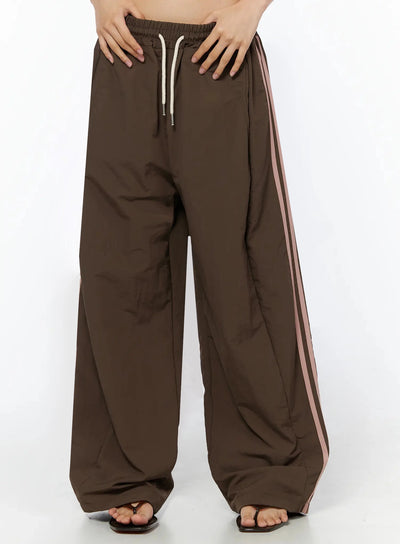 LEWKIN Contrast Stripe Track Pants IL509 Brown S/M front close-up on model showing cream drawstring elastic waistband and pink side stripes, nylon fabric