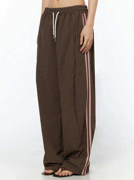 Contrast Stripe Track Pants IL509 Brown side-view waist-to-hem shot on model highlighting pink double stripe along outer leg seam and elastic waistband