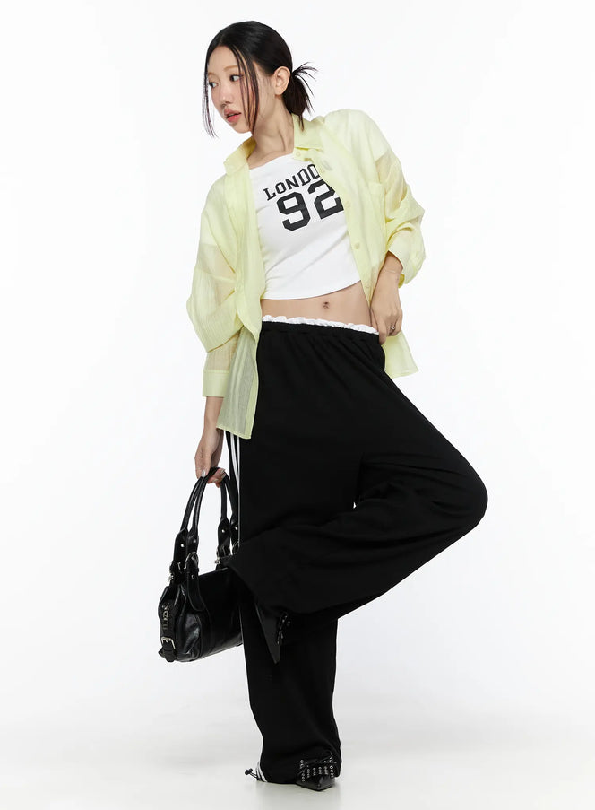 Contrast Stripe Wide Leg Sweatpants CL524 Black full-body shot on model styled with yellow sheer shirt and white graphic crop top holding black bag with leg raised