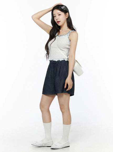 Contrast Trim Floral Tank Top IU525 Light beige three-quarter side model shot hand raised to hair showing ruffle straps and floral texture with denim shorts