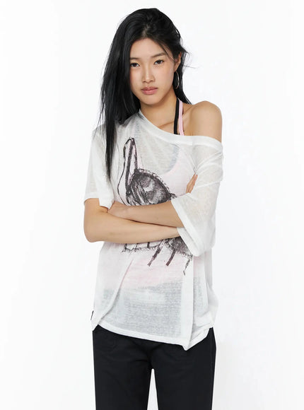 Corset Graphic Off-Shoulder Oversized Tee IL516 White front shot model arms crossed sheer tee corset sketch graphic off-shoulder styled with pink halter bralette black pants