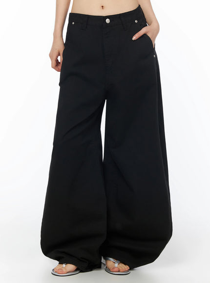 Cotton Balloon Pants IL502 Black front model shot, hands in pockets, ultra-wide balloon legs in cotton fabric with silver hardware details, silver sandals
