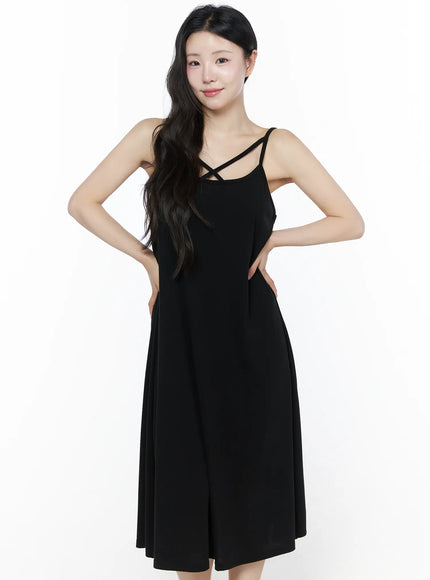 Criss-Cross Strap Maxi Dress IU525 Black front view on model with hands on hips smiling, cross-strap neckline detail visible, A-line midi length