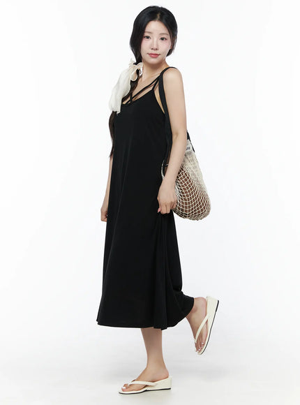 Criss-Cross Strap Maxi Dress IU525 Black side view styled on model carrying mesh net bag with ivory ribbon hair accessory and white wedge flip-flops