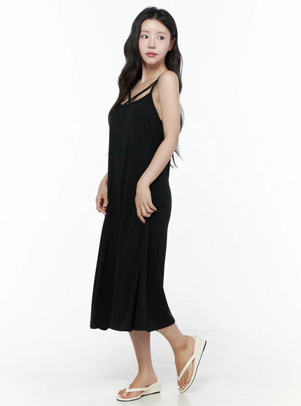 Criss-Cross Strap Maxi Dress IU525 Black side view full-length on model looking up, showing A-line silhouette flare and cross-strap neckline with white sandals
