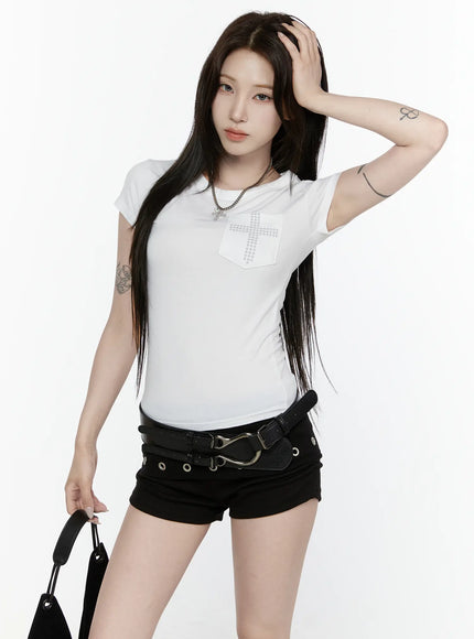 Cross Detail T-Shirt IL522 White front model shot, one hand in hair, studded cross chest pocket with chain necklace, black double-belt shorts and mini bag