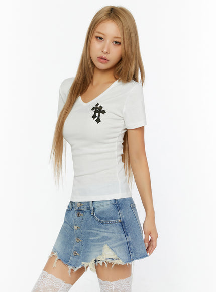 Cross Detail V-Neck Tee IL524 White angled front shot on model gazing forward, black cross patch detail at chest, V-neck slim ribbed fit styled with denim skirt