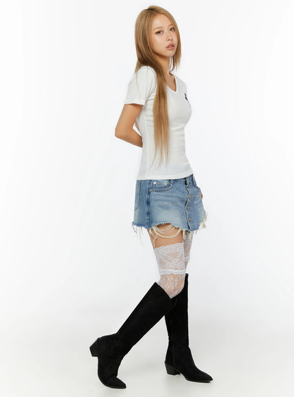 Cross Detail V-Neck Tee IL524 White side shot on model walking pose, black cross patch visible at chest, slim ribbed V-neck tee styled with distressed denim skirt